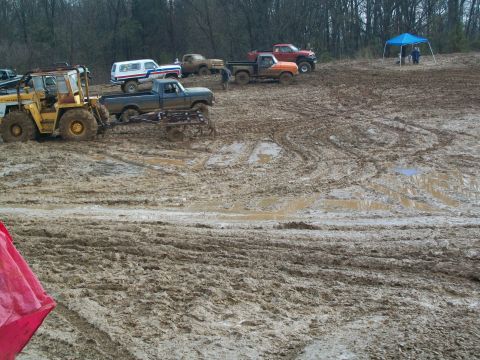 1979 Ford F-250 - Multiple trucks and a tractor are stuck in a very muddy field with a blue tent in the background.