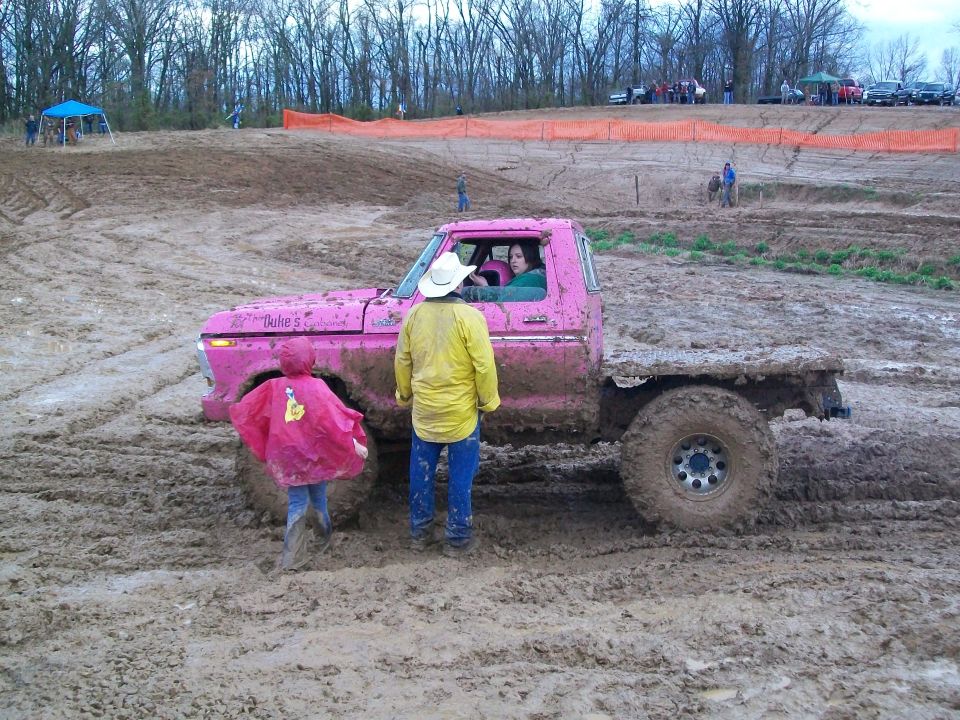 Pink pickup truck stuck in mud with people around. Text on door reads 'Dulie's'