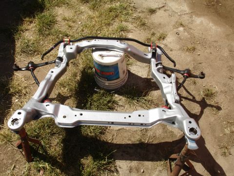 1995 Ford Taurus - Front subframe assembly with sway bar and control arms, resting on stands outdoors.