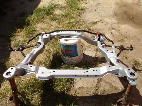 1995 Ford Taurus - A car's front subframe assembly, including control arms and sway bar, is shown outdoors.