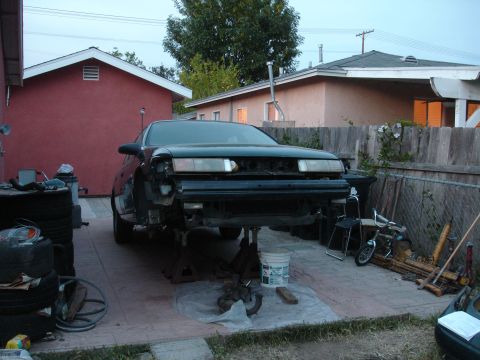 1995 Ford Taurus - Front view of a 1995 Ford Taurus on jack stands, undergoing repairs with its bumper and grille removed.