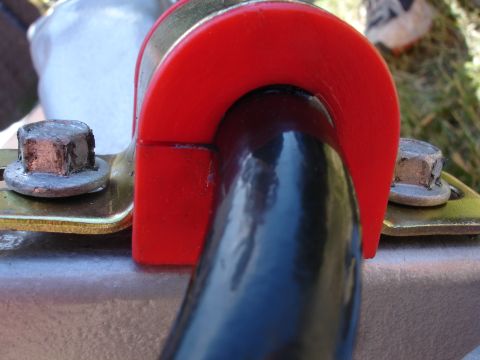 1995 Ford Taurus - Close-up view of a red polyurethane sway bar bushing clamping a black sway bar, secured by bolts.