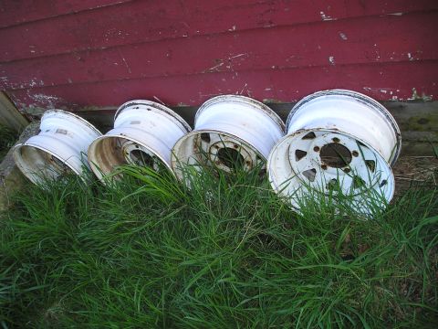 1986 Ford Bronco II - Several old white steel wheels are stored in the grass next to a red wooden wall.