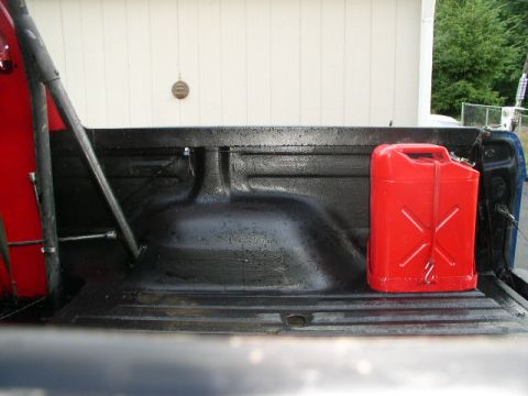 1979 Ford Bronco - A red jerry can is secured in the bed of a truck, next to a roll bar.