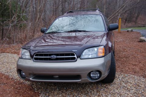 2001 Ford Crown Victoria - A maroon and tan Subaru Outback is parked outdoors, showing its front grille and headlights.