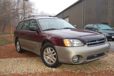 2001 Ford Crown Victoria - Maroon and tan Subaru Outback Wagon parked on gravel in front of a building. A dark SUV is in the background.