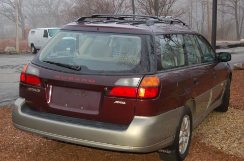 2001 Ford Crown Victoria - A maroon Subaru Outback wagon is parked on a gravel lot with a white van in the background.