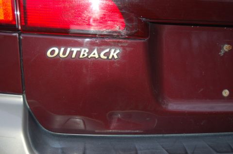 2001 Ford Crown Victoria - Rear view of a red Subaru Outback, showing the "OUTBACK" badging and a damaged taillight.
