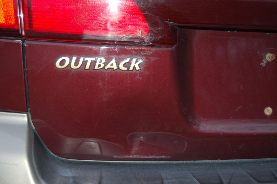 Red Subaru Outback rear with "OUTBACK" badge and damaged taillight