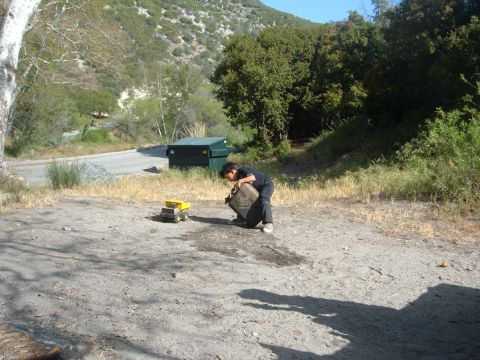 1988 Ford Bronco - Outdoor canyon scene at a dirt pullout beside a paved road: a child crouches while lifting a metal jerry can next to a small yellow toy tru…