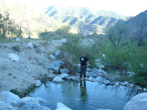 1988 Ford Bronco - A man in a black T-shirt, camo pants and a cap stands at the edge of a clear creek pool in a rocky canyon, reflected in the water, with bru…