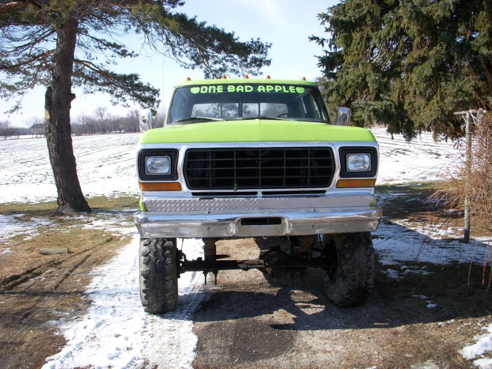 Front view of a lifted, lime green pickup truck with a black grille and chrome bumper. Decal on windshield reads 'ONE BAD APPLE'