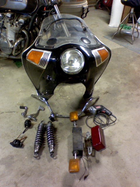 1980 Yamaha XS1100 - Disassembled motorcycle parts including a front fairing, handlebars, shocks, and turn signals are laid out on the floor.