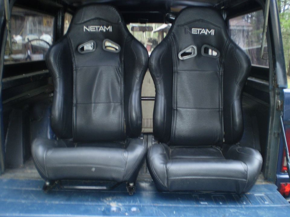 Two black Netami racing seats in the bed of a blue vehicle
