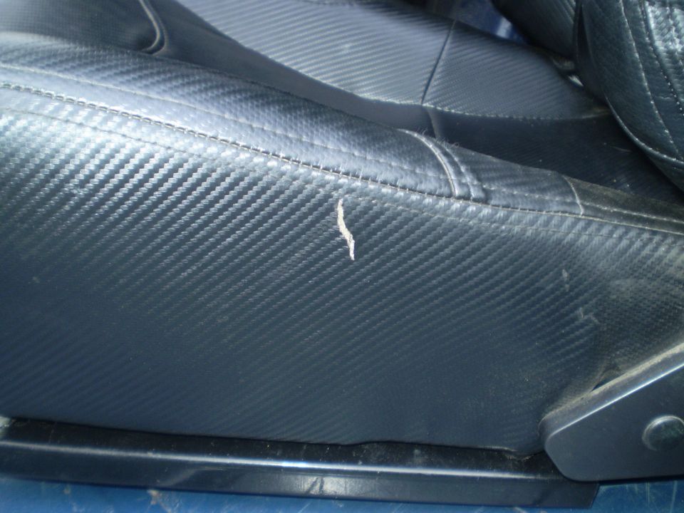 Close-up of a black car seat with carbon fiber pattern and a small tear on the side