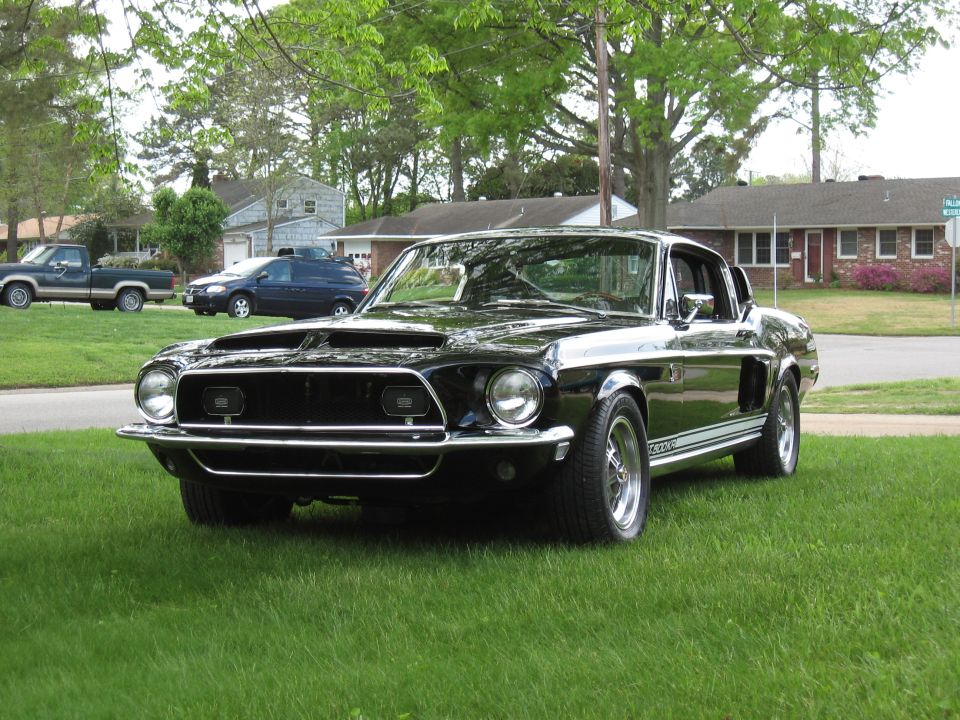 Black 1968 Shelby GT500 parked on grass, front 3/4 view, with racing stripes