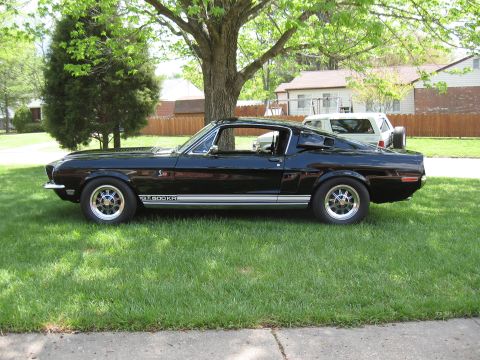 1968 Shelby GT500 - A black 1968 Shelby GT500 is parked on a grassy lawn, showing its side profile and distinctive GT500KR stripe.