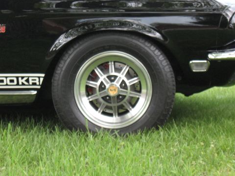 1968 Shelby GT500 - A close-up shot focuses on the wheel and fender of a black vehicle, with grass in the foreground.