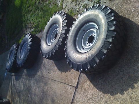 1985 Ford F-150 - A set of four off-road tires and rims are laid out on a concrete surface with grass in the background.
