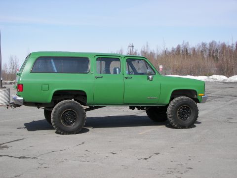 1990 Chevrolet Suburban - This lifted green Chevrolet Suburban is shown from the side under a clear sky.