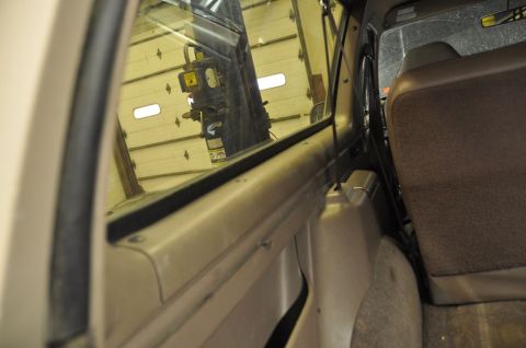 1996 Ford Bronco - View from inside a vehicle, showing the interior trim and a reflection of a garage in the window.