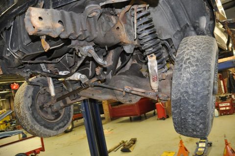 1996 Ford Bronco - The front suspension and axle of a 1996 Ford Bronco are visible from below while on a vehicle lift.