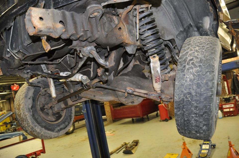 Undercarriage of a 1996 Ford Bronco on a lift, showing suspension and front axle components