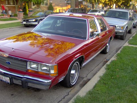 1990 Ford Crown Victoria LTD - A red sedan is parked on the side of a residential street, with other vehicles visible behind it.