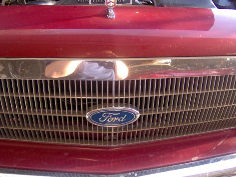 1990 Ford Crown Victoria LTD - Close-up of a Ford emblem on a red vehicle's front grille.