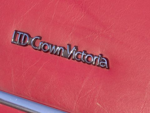 1990 Ford Crown Victoria LTD - Close-up of the LTD Crown Victoria badge on a red background.