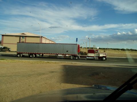2009 Kenworth T800 - A semi-truck with a long silver trailer drives down a highway next to a hotel.
