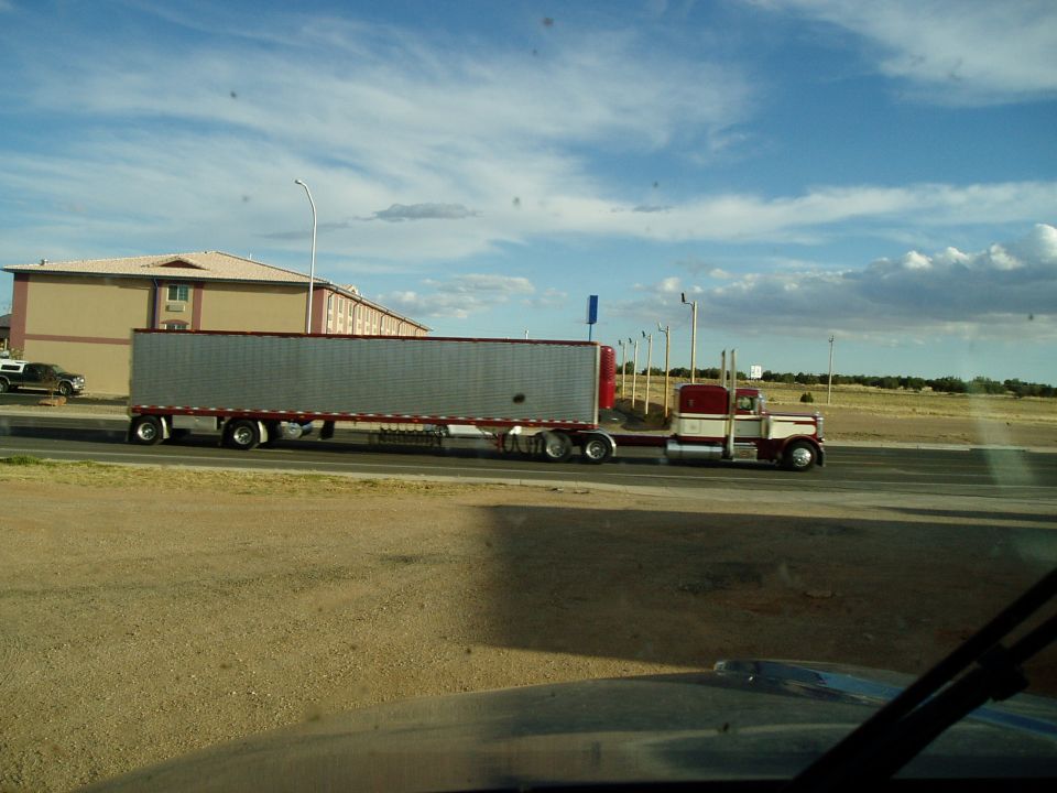 Side view of a white and maroon semi-truck pulling a silver trailer