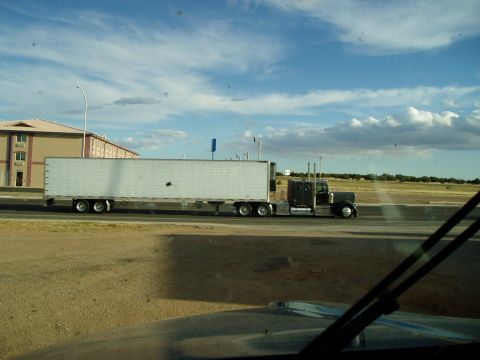 2009 Kenworth T800 - A semi-truck and trailer travels down the highway past a hotel under a cloudy sky.
