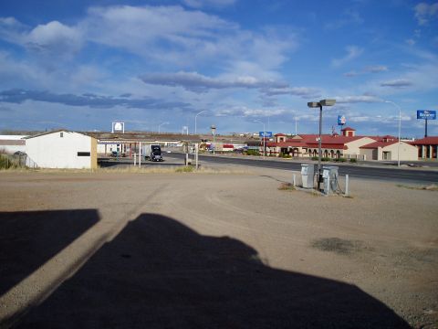 2009 Kenworth T800 - A black semi-truck is parked under a covered area at a rest stop with a hotel in the background.