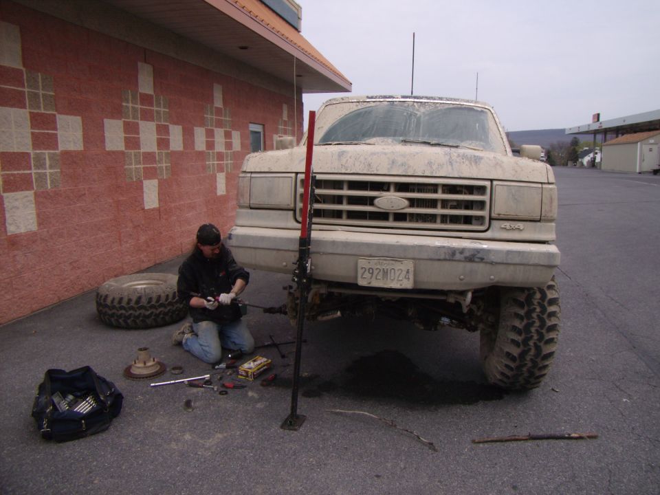 Mud-covered Ford F-Series truck being worked on by a person with tools and a spare tire nearby