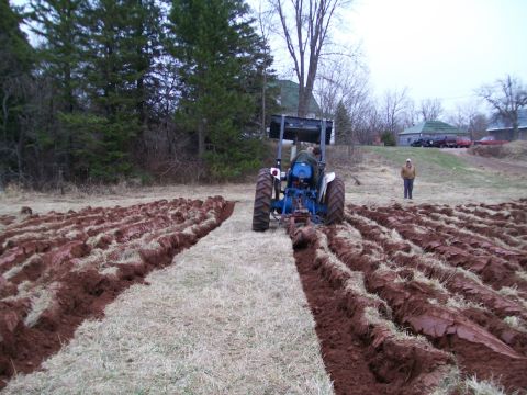 2000 Chevrolet Tahoe - A tractor is plowing a field, creating furrows in the soil. A person watches in the distance.
