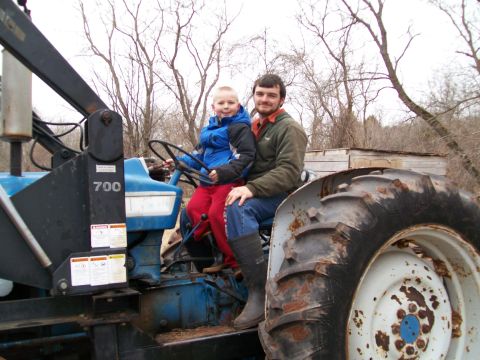2000 Chevrolet Tahoe - A man and a boy sit on a blue tractor with a loader arm in an outdoor setting.