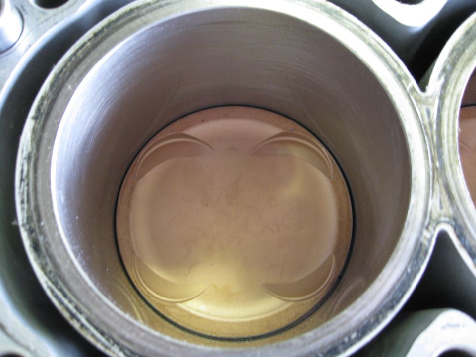 Engine cylinder with piston visible inside, showing wear marks and a metallic sheen