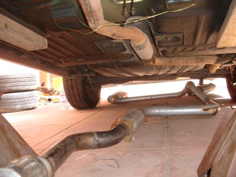 1995 Ford Taurus - The undercarriage of a vehicle is shown with the exhaust system disconnected and lying on the ground.