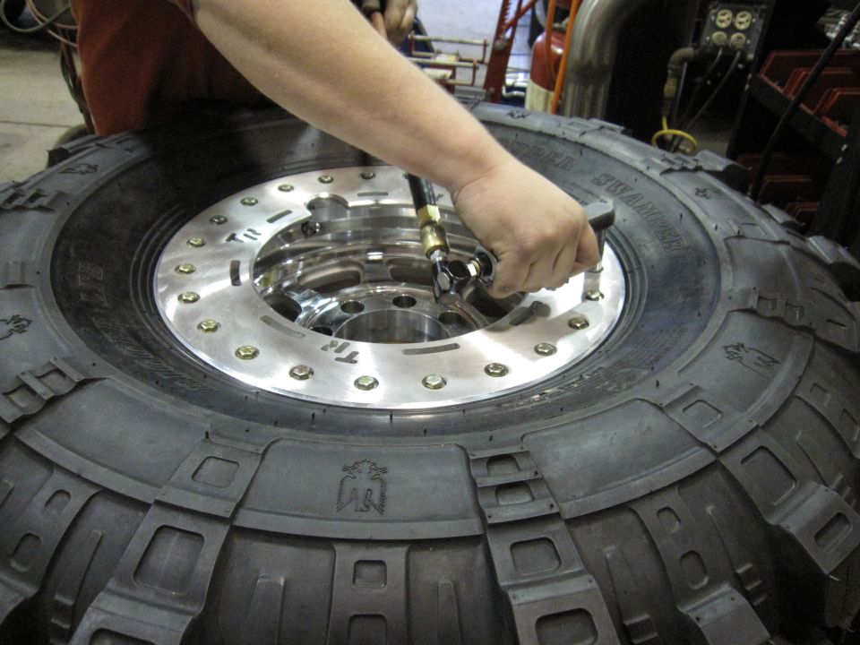 Hand using air chuck to inflate a large off-road tire mounted on a polished metal wheel