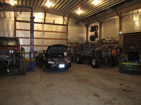 1992 Ford Bronco - Multiple vehicles are present in a garage, including a red Jeep, a dark sedan, and a custom-built Jeep.