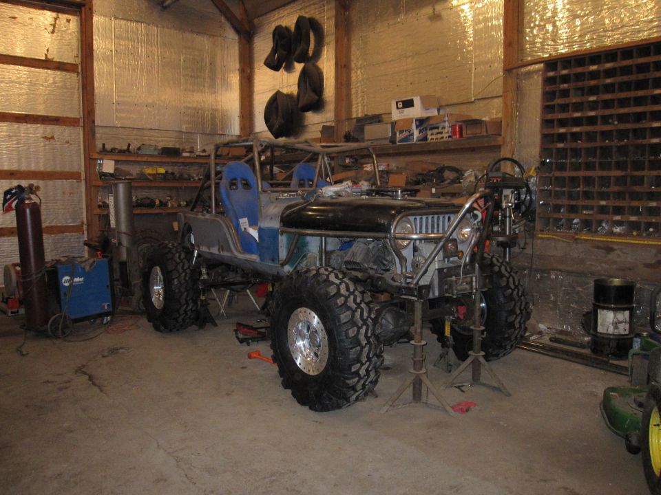 Custom off-road vehicle with roll cage and large tires, in a garage