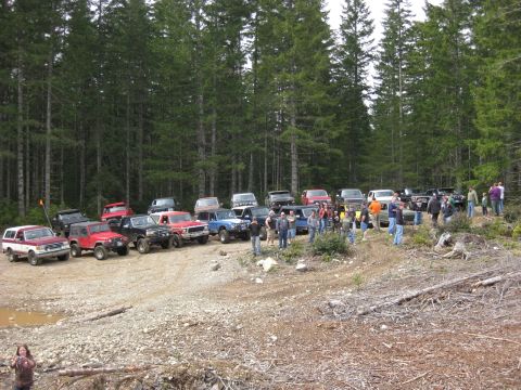 1979 Ford Bronco - A large group of off-road vehicles and people are gathered in a wooded area, likely for an outdoor event or trail ride.