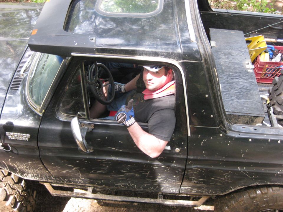Black 1978 Ford Bronco with mud splatters, driver wearing a neck brace and gloves