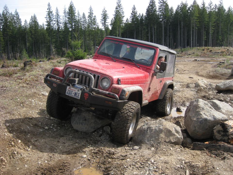 Red Jeep Wrangler navigating rocky terrain, license plate 207-WEE