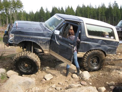 1979 Ford Bronco - A 1979 Ford Bronco navigates rocky terrain, its driver's door open as a person exits.