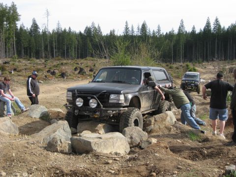 1979 Ford Bronco - Black Ford Bronco is being helped over rocks by people while another SUV follows behind.