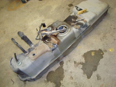 2007 Ford Mustang - A removed fuel tank assembly, showing the fuel pump and associated lines, rests on a concrete floor.