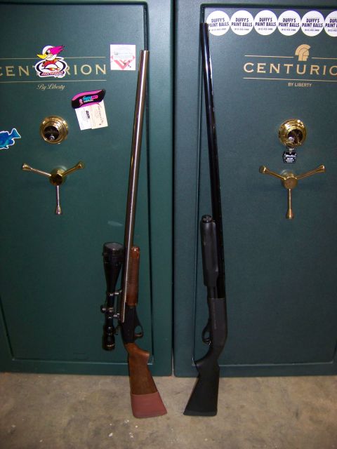 1995 Mercury Grand Marquis - Two rifles are displayed leaning against two large green gun safes, one with a scope and wood stock, the other a black pump-action.