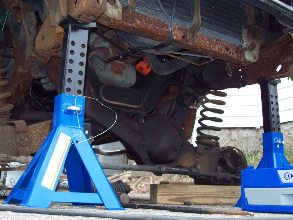 Underside of a truck supported on blue jack stands showing coil spring